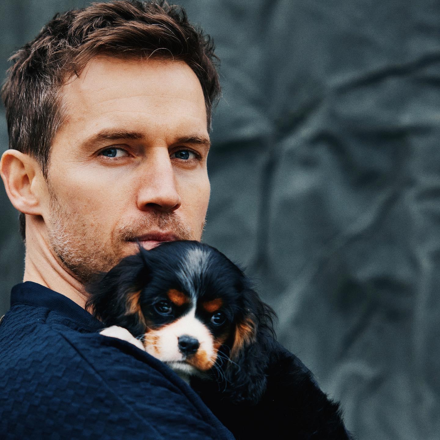 El modelo Andrew Cooper en una imagen de perfil con un cachorrito en brazos