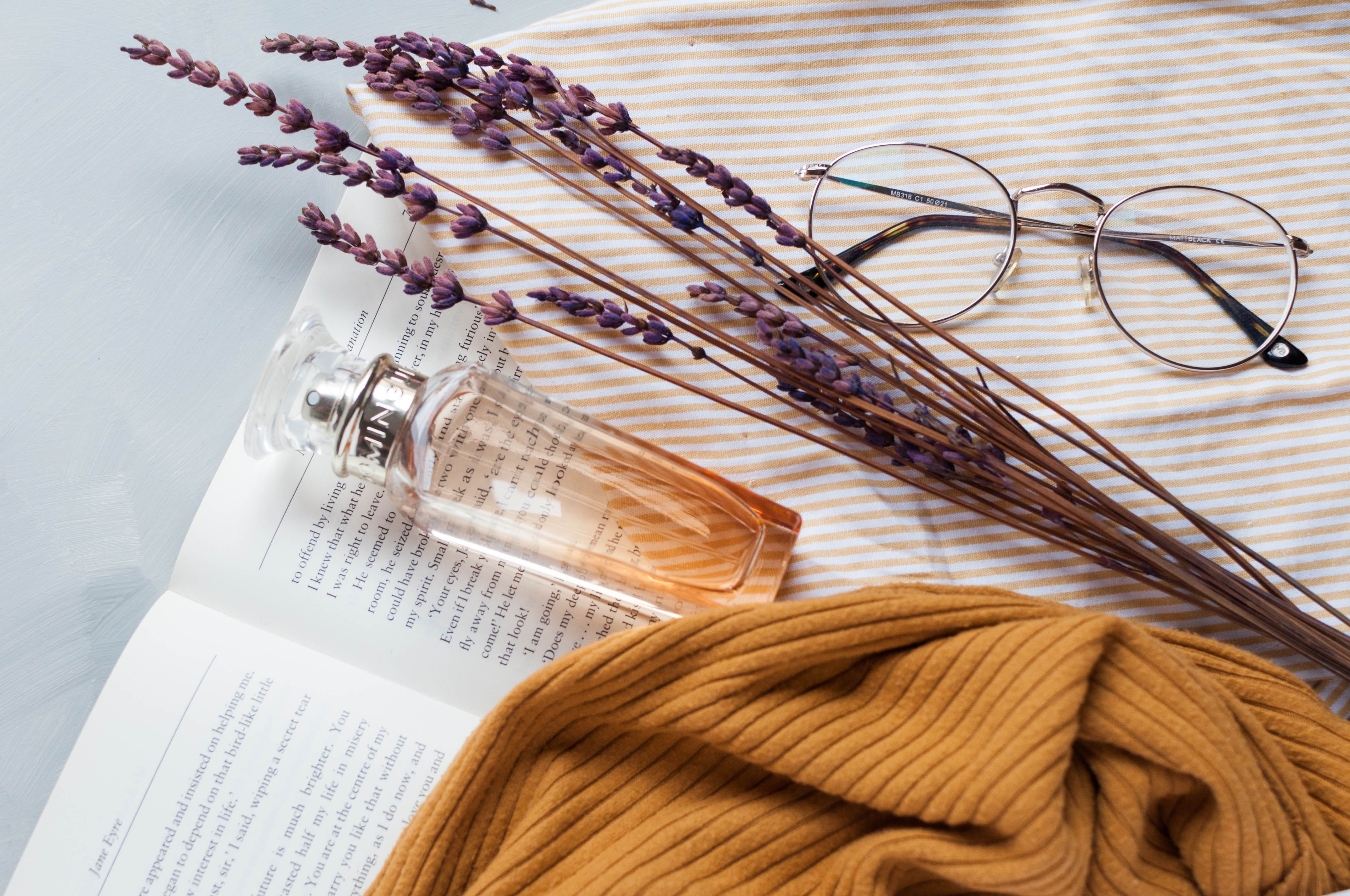 frasco de perfume sobre un libro al lado de unas gafas y un ramo de lavanda
