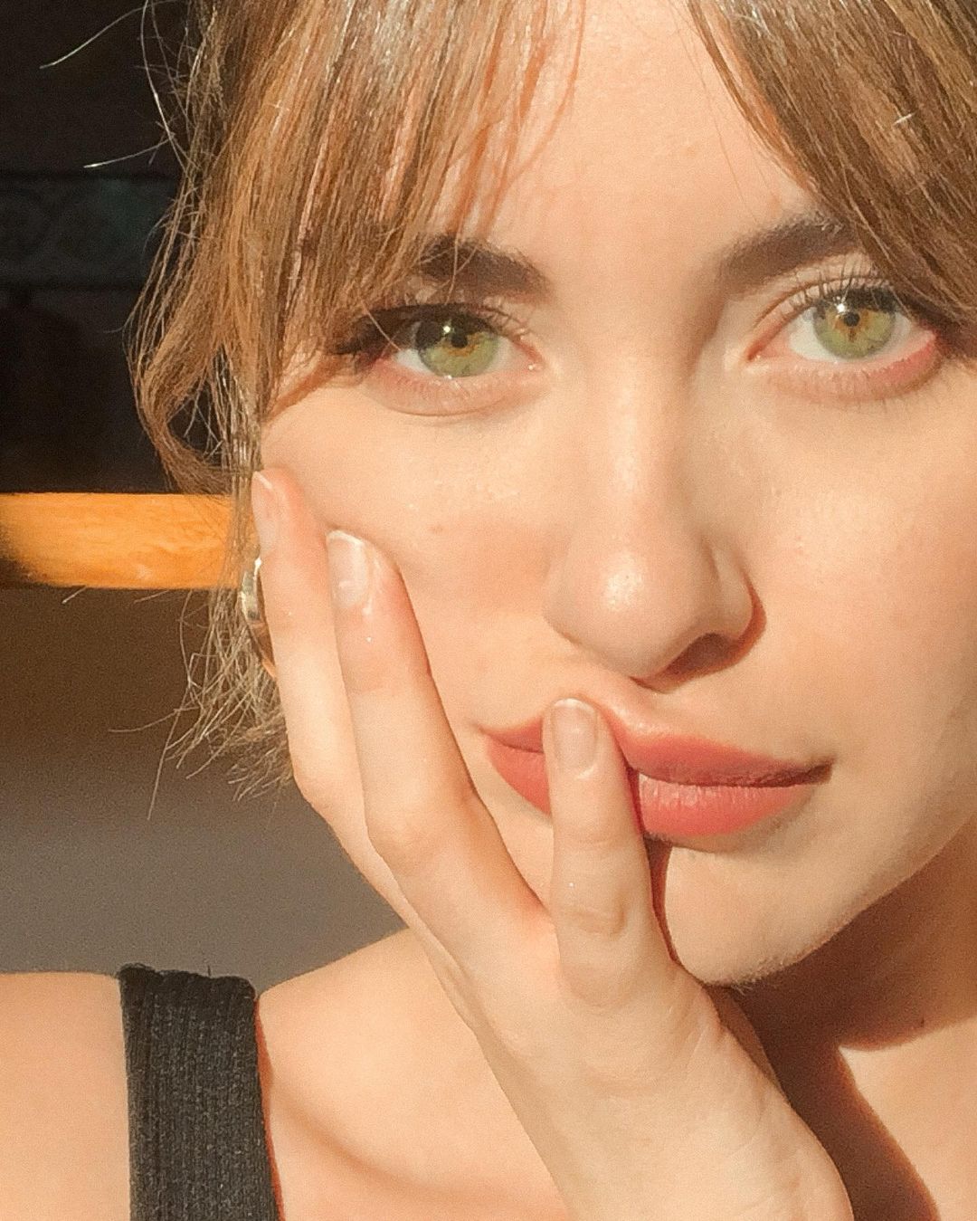 Imagen de un plano corto del rostro de una mujer con la mano sobre la mejilla, ojos verdes y flequillo abierto