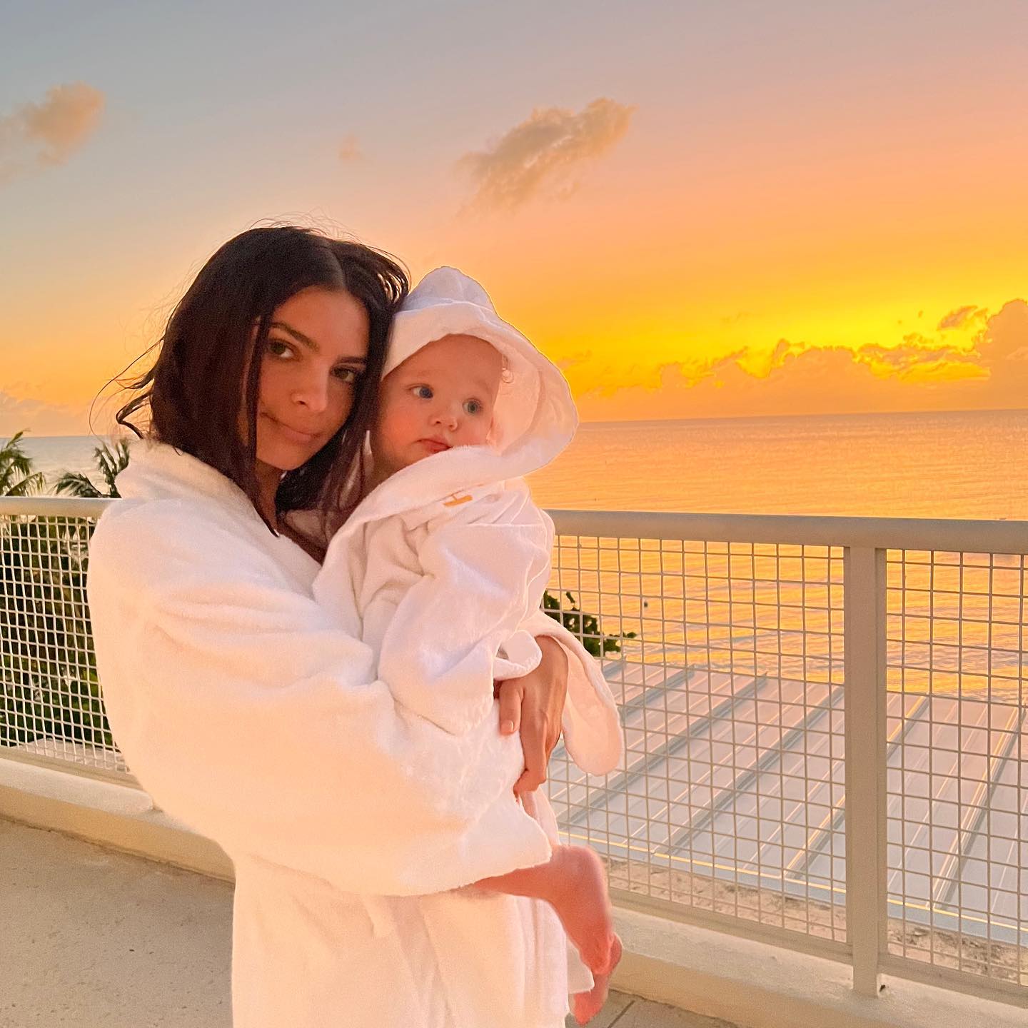 La modelo Emily Ratajkowski con su bebé en brazos, ambos en albornoz, en una puesta de sol