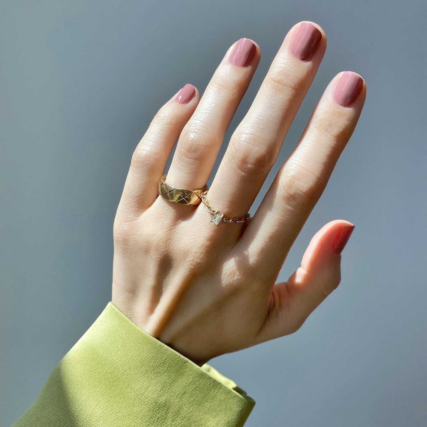 Imagen de una mano con una manicura en color nude y anillos en dorado