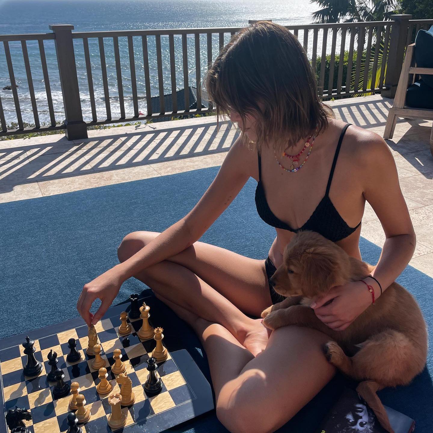 La modelo Kaia Gerber sentada en bikini jugando al ajedrez con un perro a su lado