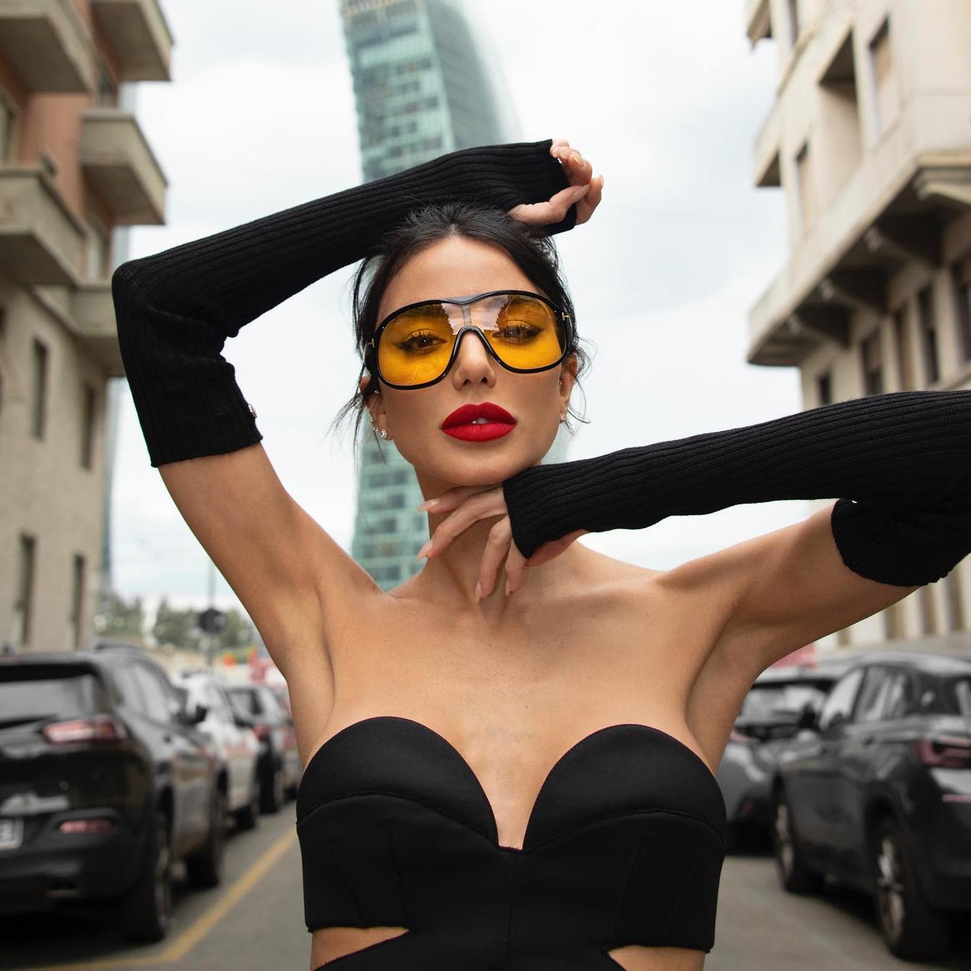 La influencer italiana Chiara Biasi posa con un top negro con guantes, unas gafas con cristal naranja y los labios rojos.