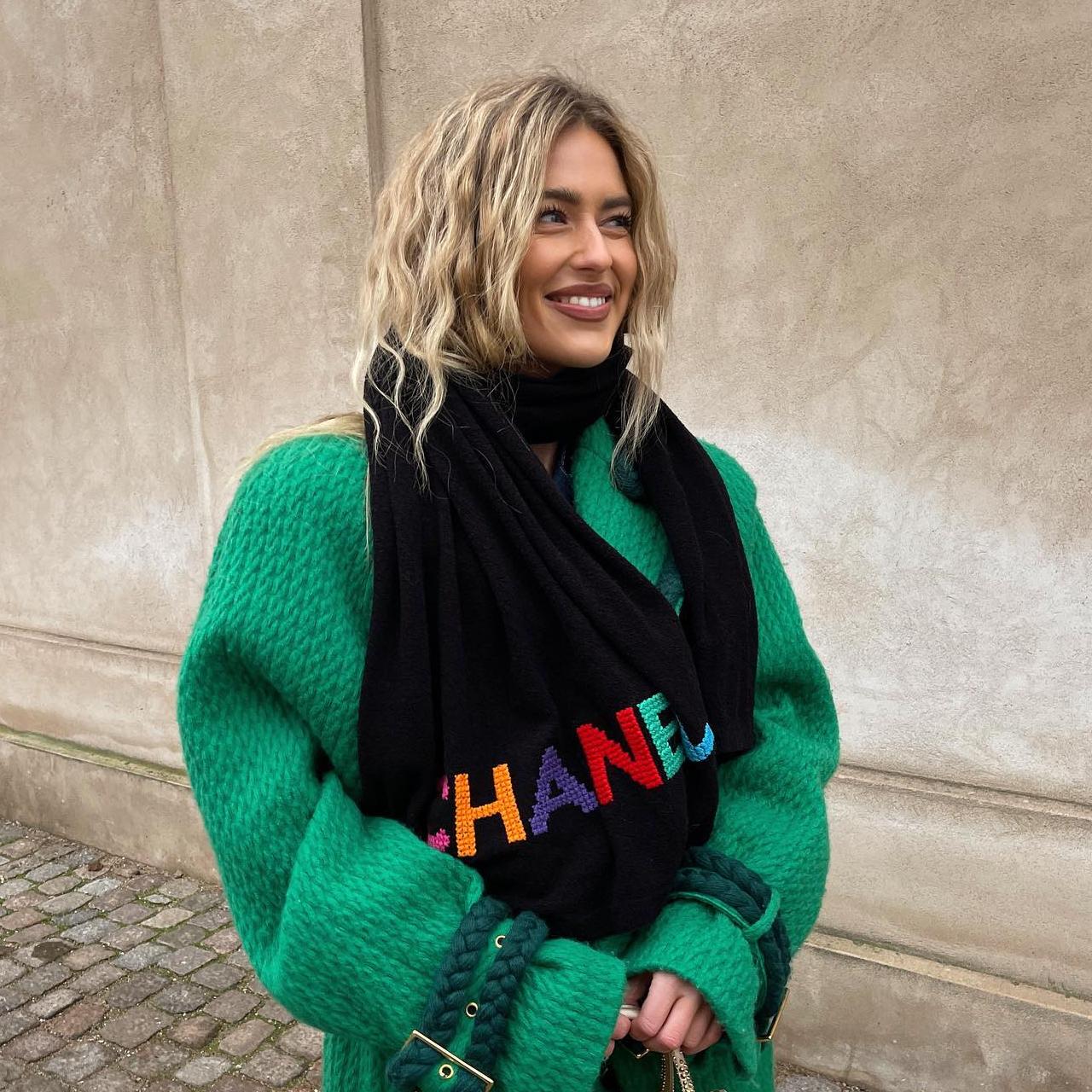 La influencer Emili Sindlev posa mirado hacia un lado con ropa de invierno, el pelo ondulado y un maquillaje natural dejando ver los dientes al sonreir