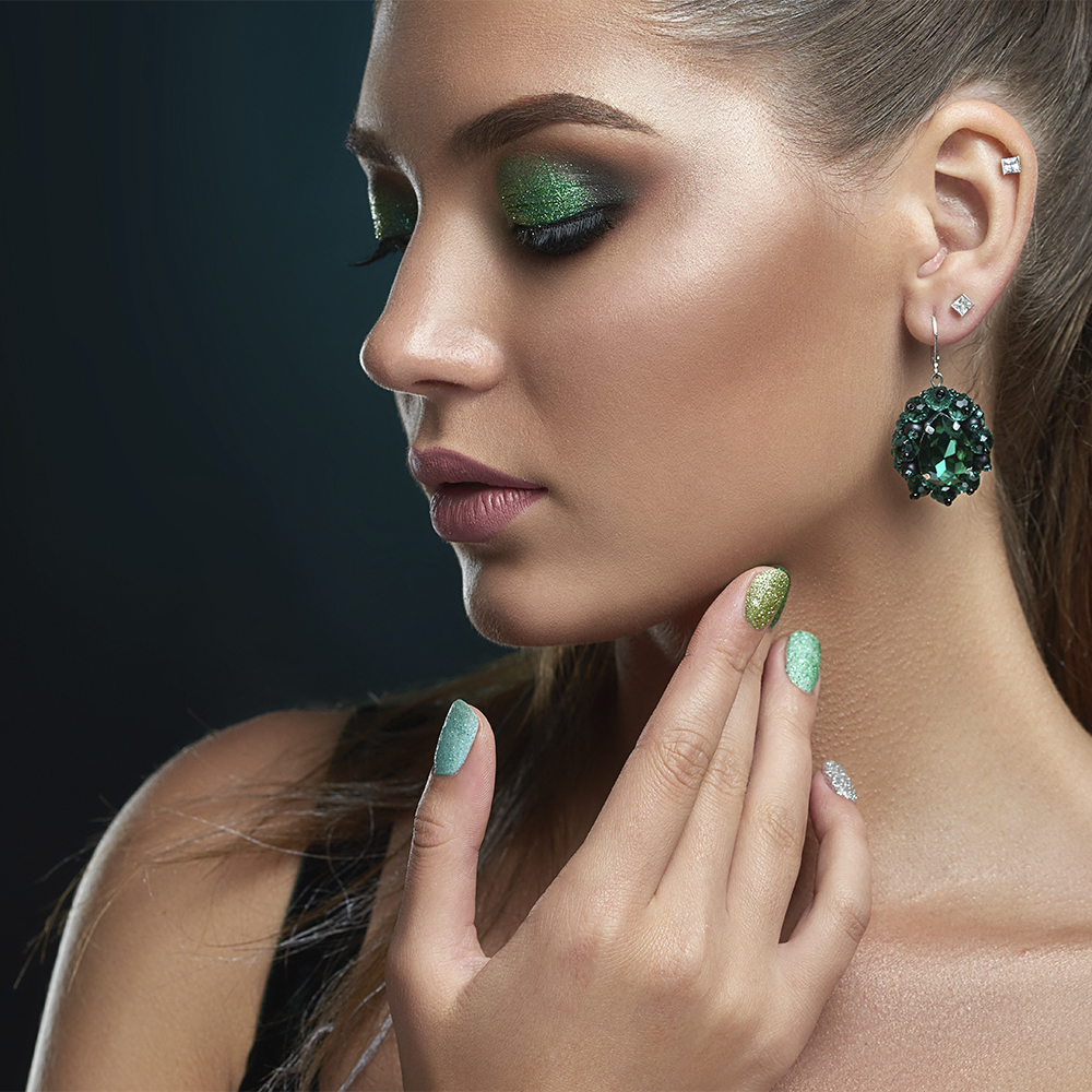 Una chica de perfil con un maquillaje marcado, sombras y manicura en tonos verde intenso