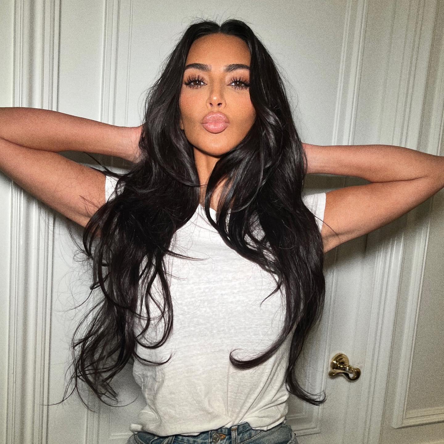 Kim Kardashian posa con las manos sobre la cabeza, el pelo suelto y un maquillaje en tonos nude