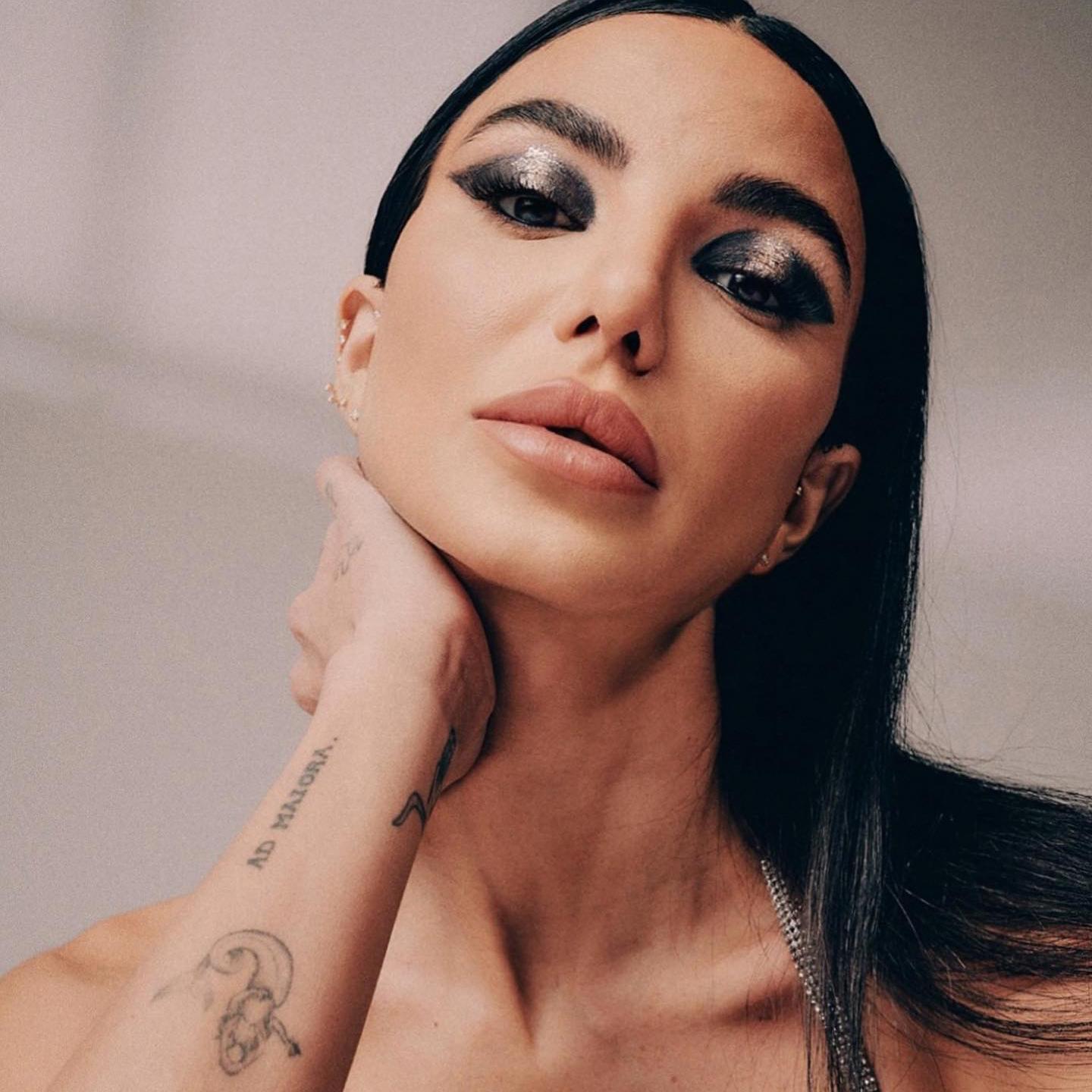 La influencer Chiara Biasi posa con los ojos muy maquillados en un tono metalizado y una mano apoyada sobre el cuello con tatuajes en el brazo