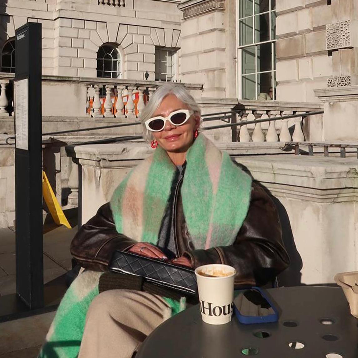 La influencer Grece Ghanem con el pelo corto blanco y flequillo de lado posa sentada en una terraza al sol
