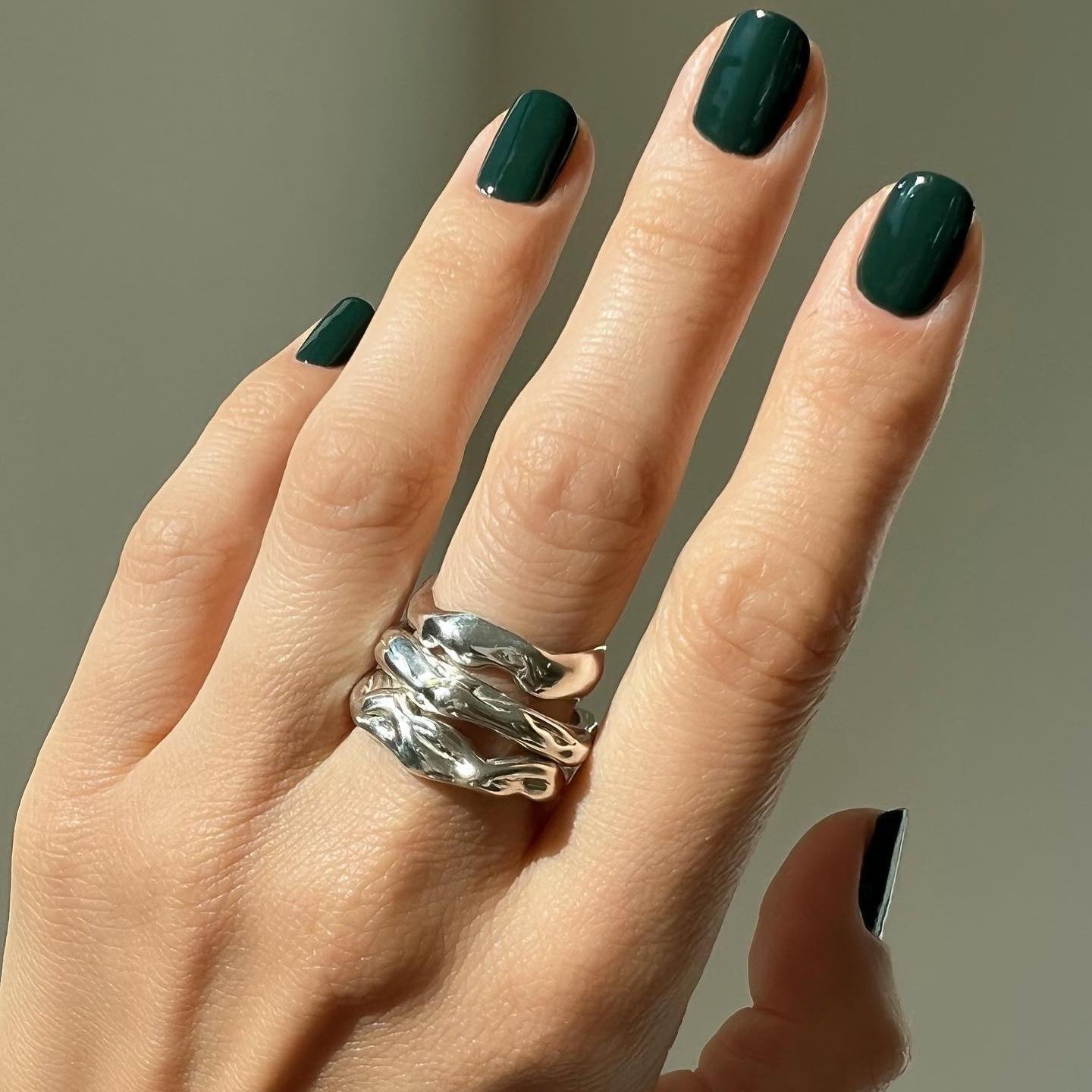 Manicura en color verde oscuro, sencilla y elegante y combinada con un maxi anillo en plata